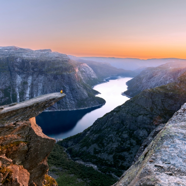 Fjordlandschaft mit Person auf einer Felsklippe bei Sonnenuntergang.