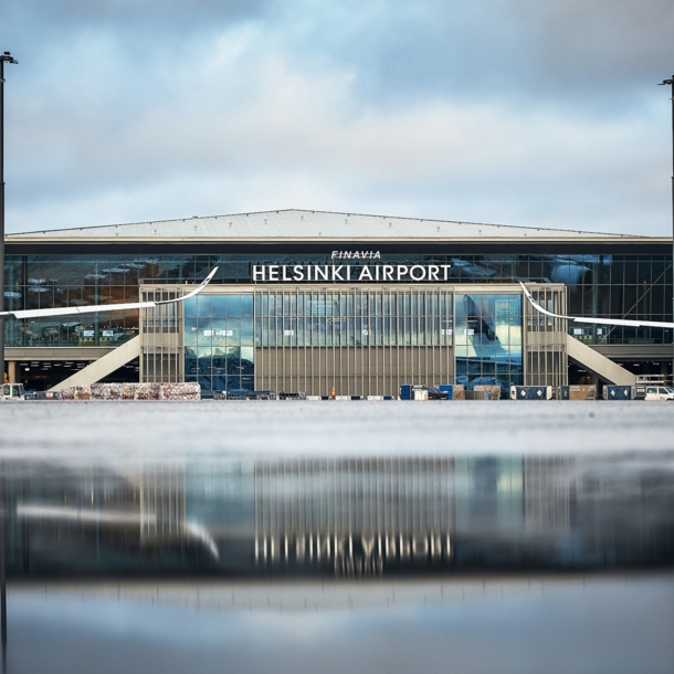 Helsinki Flughafenterminal mit Flugzeugen, im Vordergrund Spiegelung des Gebäudes auf nassem Rollfeld.