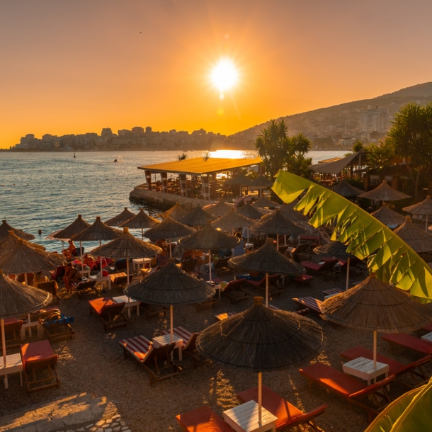 Sandstrand mit Sonnenliegen und Sonnenschirmen aus Stroh bei Sonnenuntergang.