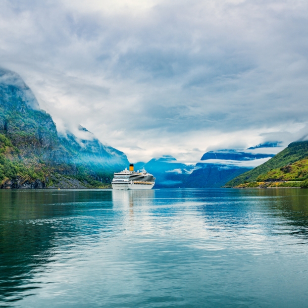 Kreuzfahrtschiff in wolkenverhangener Fjordlandschaft.