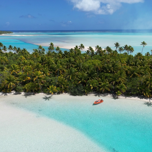 Südseeinsel mit Palmenwald an einer trürkisblauen Lagune mit weißem Sandstrand.