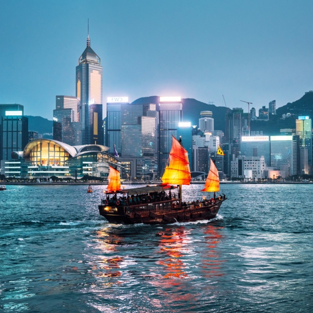 Rote chinesische Dschunke auf dem Wasser vor der Skyline Hongkongs bei Nacht.