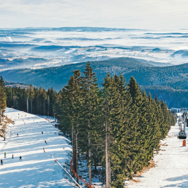 Skilift, der im Riesengebirge über eine Skipiste und Wald verläuft, im Hintergrund Berge.