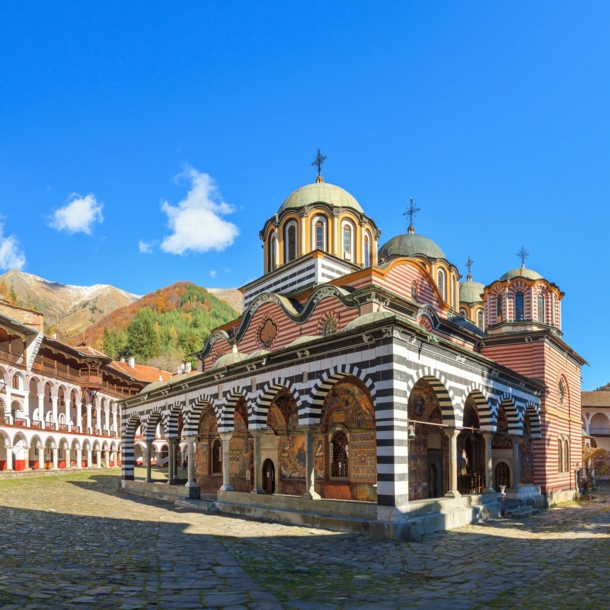 Orthodoxe Klosteranlage mit farbenfrohen Gebäuden im Gebirge unter blauem Himmel.