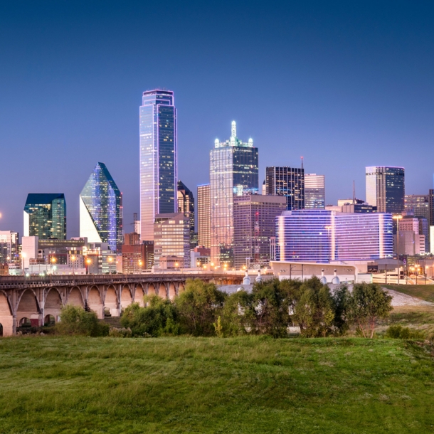 Skyline von Dallas mit Wolkenkratzern hinter einer Grünfläche mit Brückenbauten bei Abenddämmerung.