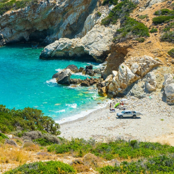 Ein Van steht auf einem Sandstrand in einer kleinen mediterranen Felsbucht mit türkisblauem Wasser.