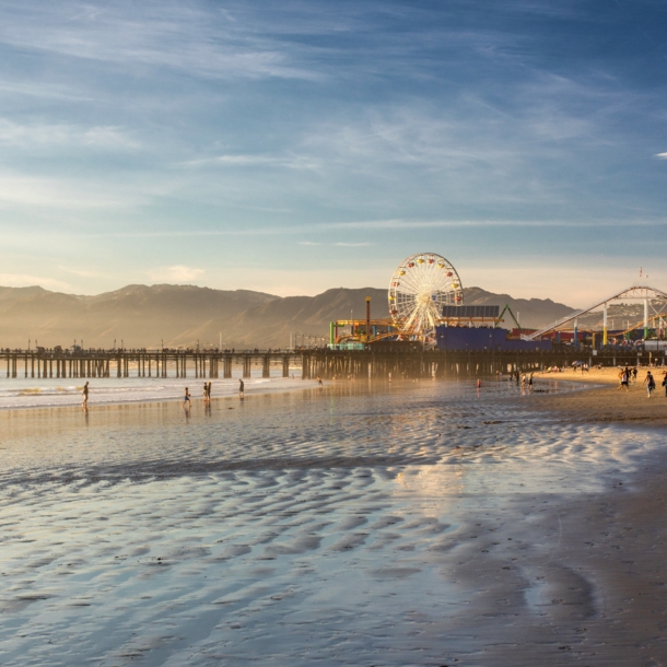 Ein Pier mit Freizeitpark an einem weitläufigen Sandstrand bei Sonnenuntergang.