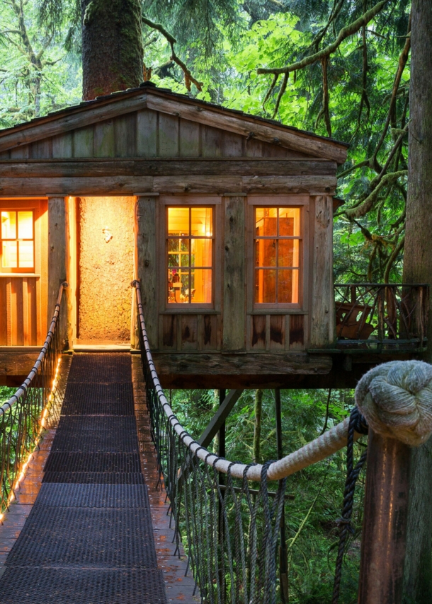 Ein beleuchtetes Baumhaus mit Hängebrücke im Wald