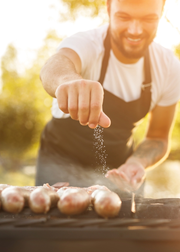 Mann streut Salz auf Würstchen die auf einem Grill liegen