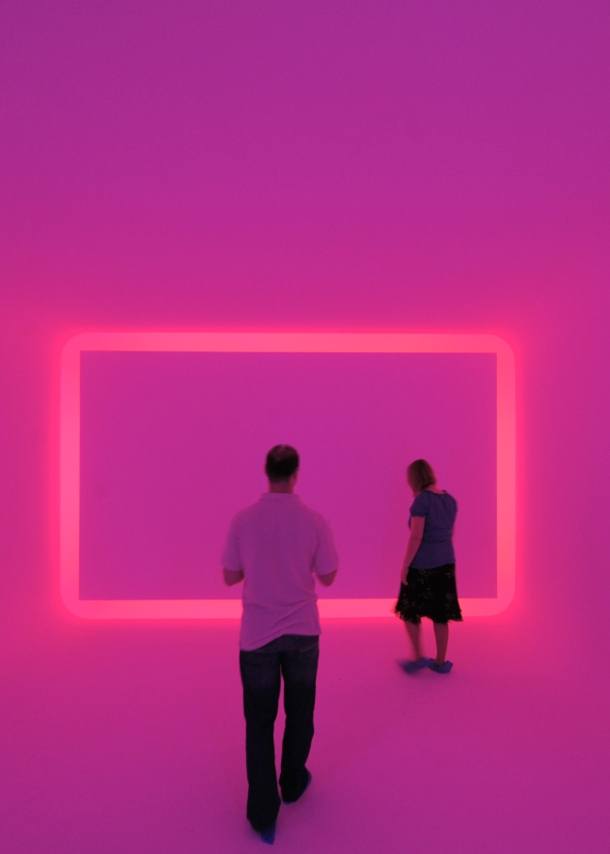 Zwei Museumsbesucher:innen in einem Raum, der pink beleuchtet ist