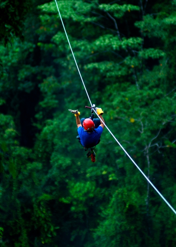 Ein Mann mit Helm gleitet an der Zipline über ein Waldgebiet