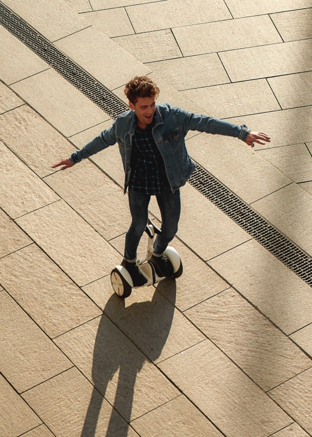 Ein lachender, junger Mann in Jeansjacke auf einem weißen Hoverboard