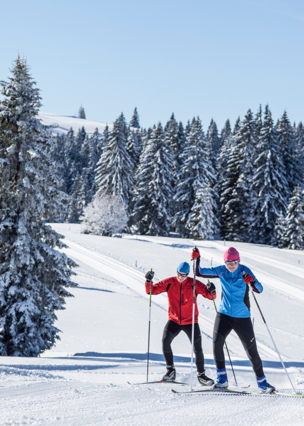 Zwei Skilanglaufende auf Loipe in hügeliger Winterlandschaft