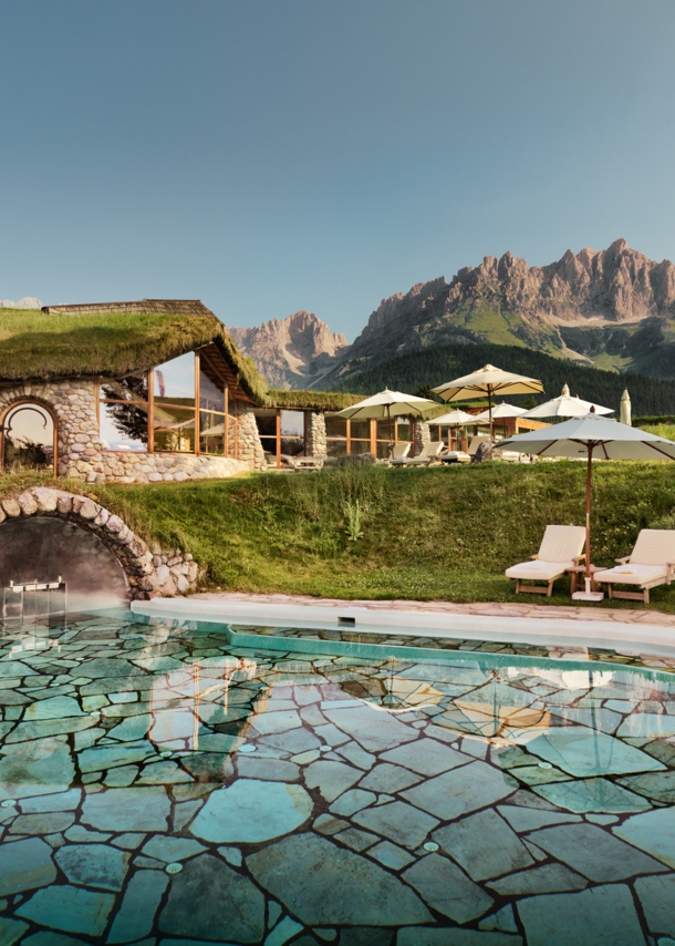 Hotelanlage mit begrüntem Dach und Liegen am Außenpool vor Bergpanorama