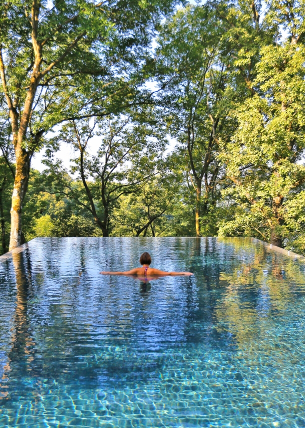 Rückansicht einer Frau im Infinity-Pool, im Hintergrund Baumkronen