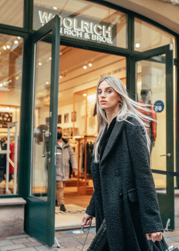 Eine Frau in langem schwarzen Mantel läuft an einem winterlichen Schaufenster vorbei