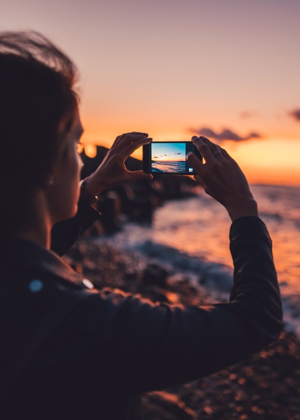 Eine junge Frau fotografiert einen Sonnenuntergang am Meer mit dem Handy