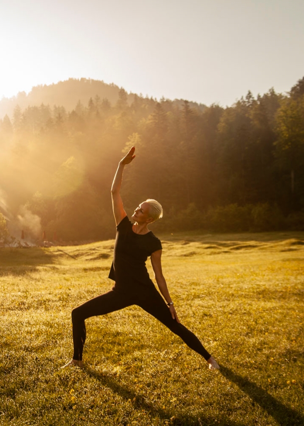 Eine Frau macht Yoga bei Sonnenaufgang und noch leichtem Nebel in einem grünen Garten