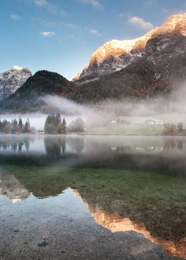 Ein See mit glasklarem Wasser über dem Nebelschwaden liegen vor Bergpanorama in der Dämmerung