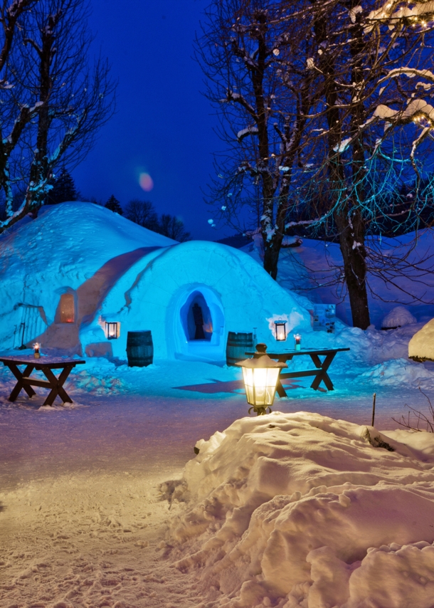 Ein Iglu in einer schneebedeckten Umgebung, daneben Tische und Bäume