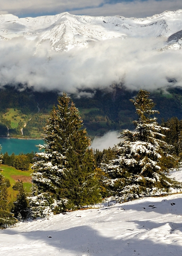 Schneebedeckte Berge, ein Bergsee und tiefhängende Wolken