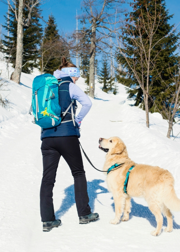 Frau mit Wanderrucksack und Hund im Schnee