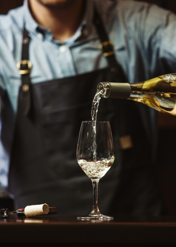 Ein Mann mit Schürze gießt Weißwein in ein Glas