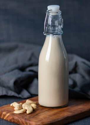 Neben einer Flasche mit Cashewmilch liegen einige Cashewnüsse.