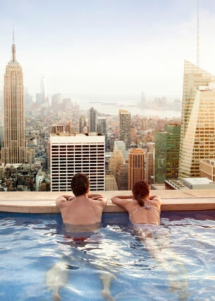 Rückansicht eines Paares in einem Rooftop-Pool, das auf die Skyline von Manhattan blickt