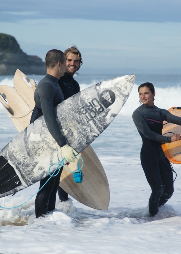 Drei Menschen stehen in Neoprenkleidung und Surfbrettern im Wasser.