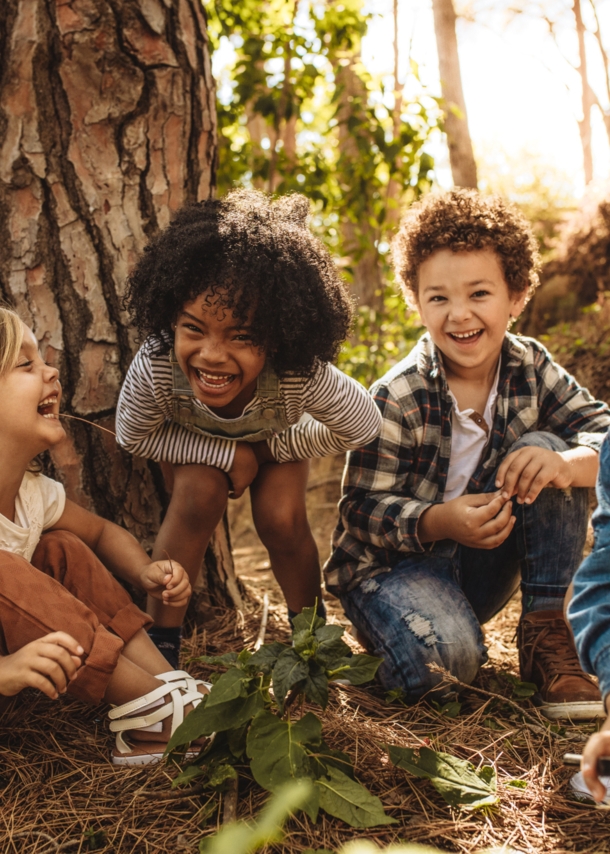 Vier fröhliche Kinder sitzen vor einem Baum im Grünen