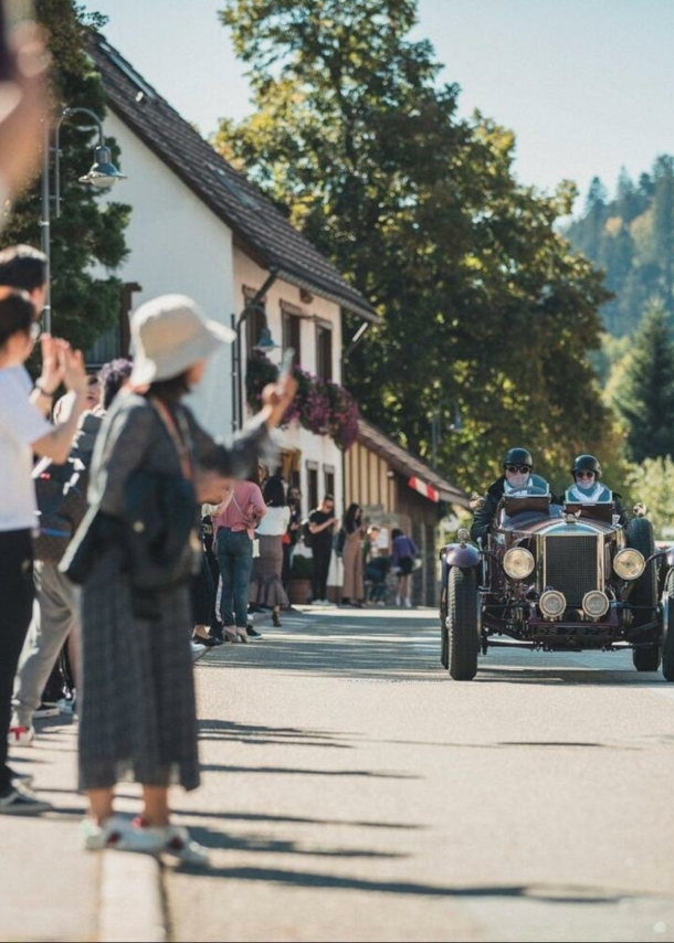 Zuschauer beklatschen Oldtimer auf einer Straße