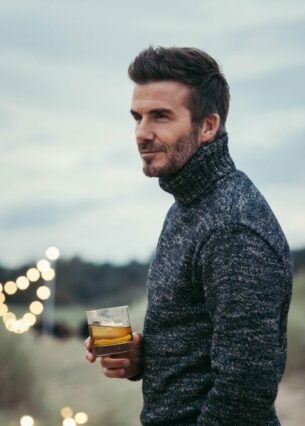 Porträtaufnahme von David Beckham in den Dünen mit einem Glas Whisky in seiner Hand