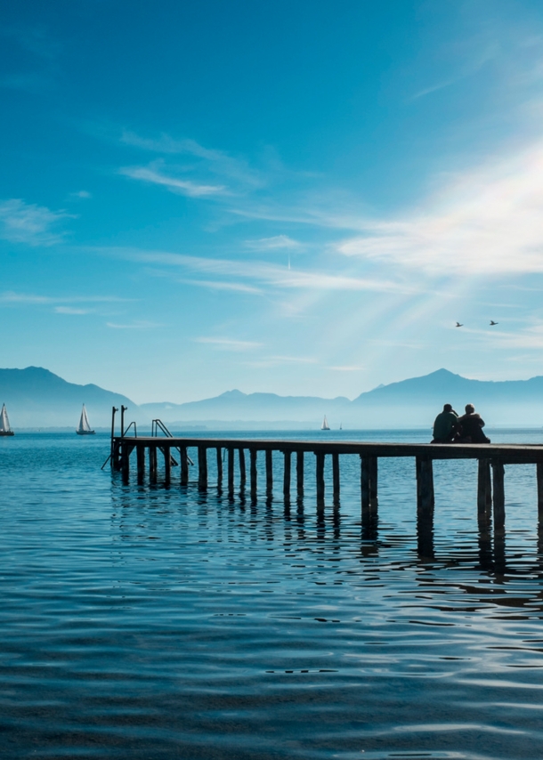 Zwei Personen sitzen auf einem Holzsteg auf dem Chiemsee