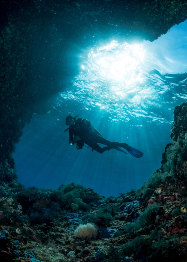 Taucher unter Wasser am Eingang einer Höhle mit Sonnenstrahlen im Hintergrund