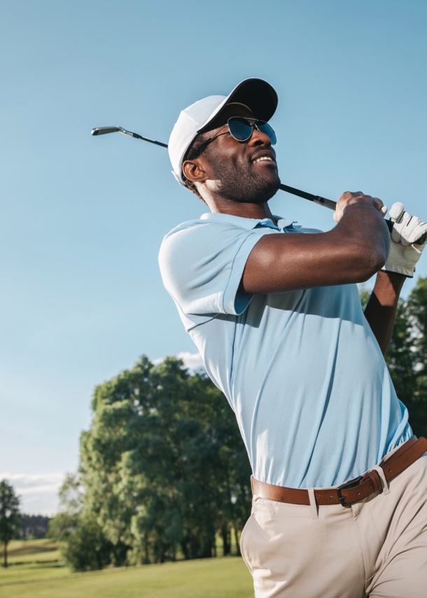 Porträt eines dunkelhäutigen Golfers in einem blauen Poloshirt beim Abschlag auf einem Golfplatz