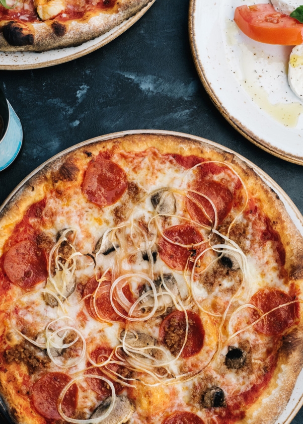 Aufsicht einer Pizza neben weiteren italienischen Gerichten und einem Glas Wein auf einem Tisch