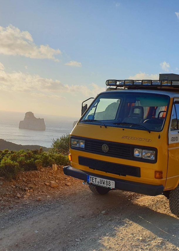 Ein gelber VW T3 auf einer Küstenstraße in den Bergen