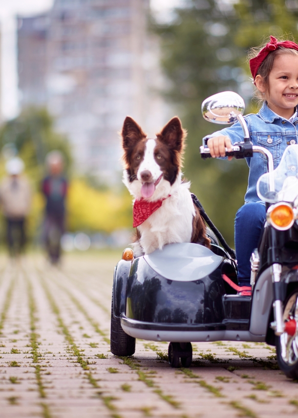 Kleines Mädchen mit Hund auf einem Kindermotorrad