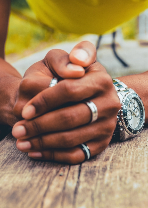 Gefaltete Männerhände mit silbernen Ringen und einer Uhr am Handgelenk