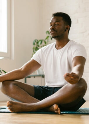 Ein Mann sitzt im Schneidersitz auf einer Yogamatte und meditiert mit einer Meditations-App