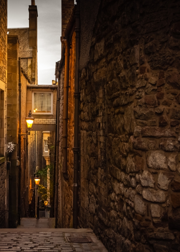 Dunkle Gasse in Edinburgh, die von Straßenlaternen schwach beleuchtet wird.