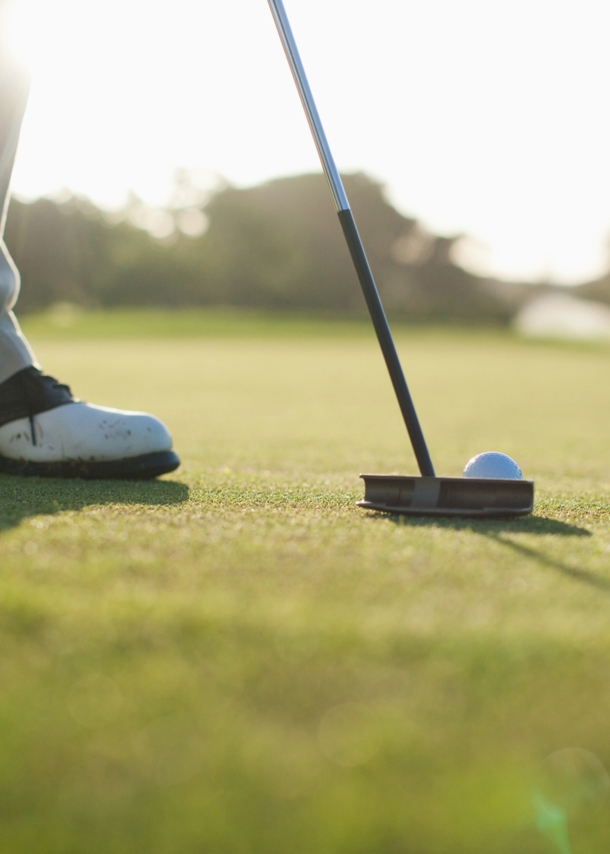 Nahaufnahme von einem Golfschläger, dahinter ein weißer Golfball auf einem grünen Rasen