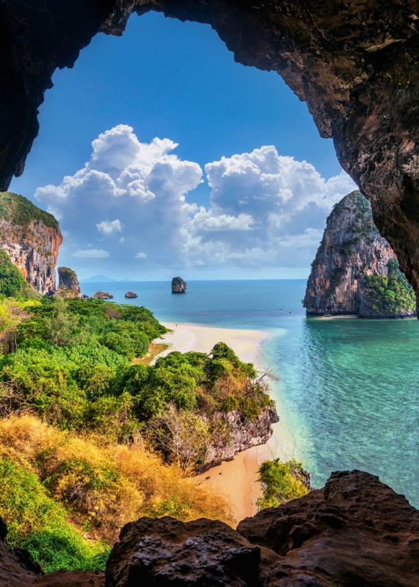 Blick aus einer Höhle auf Strand, Meer und Bäume