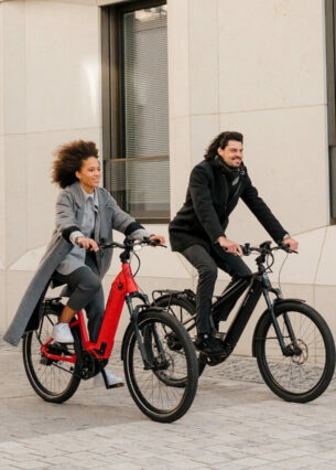 Ein Mann und eine Frau radeln auf zwei E-Bikes an einem Haus vorbei