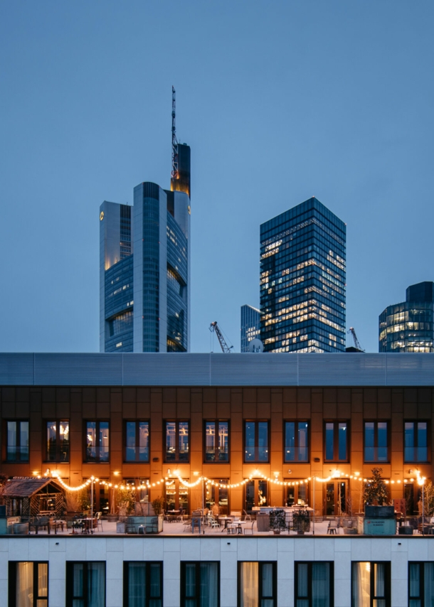 Eine beleuchtete Rooftop-Bar vor der Frankfurter Skyline bei Nacht