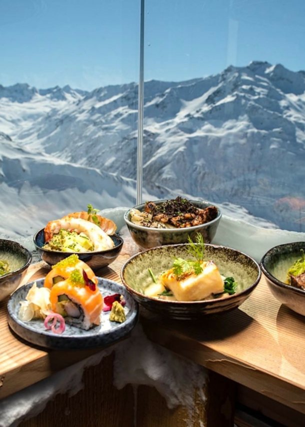 Japanisch angerichtete Teller auf einem Holztresen, im Hintergrund das Panorama von Andermatt