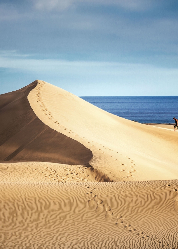 Zwei Personen wandern auf einer großen Sanddüne am Meer