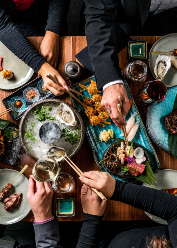 Hände nehmen mit Stäbchen Essen von Tellern in der Mitte eines Tisches