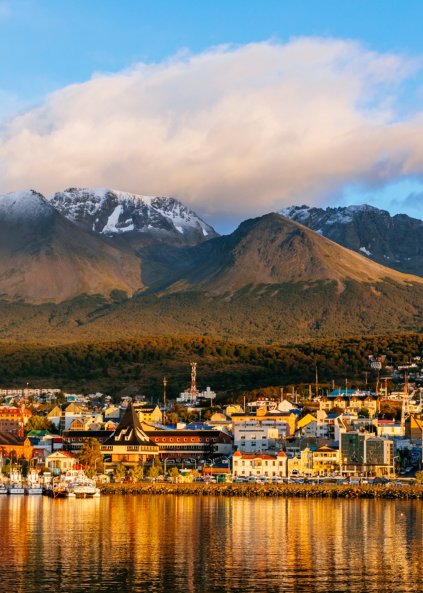 Stadtpanorama von Ushuaia am Wasser vor Bergkulisse im Sonnenuntergang